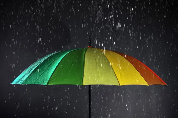 Karanlık arka planda yağmur altında parlak şemsiye — Stok fotoğraf