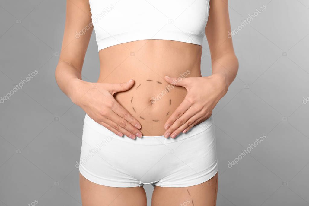 Young woman with marks on body for cosmetic surgery operation against grey background, closeup
