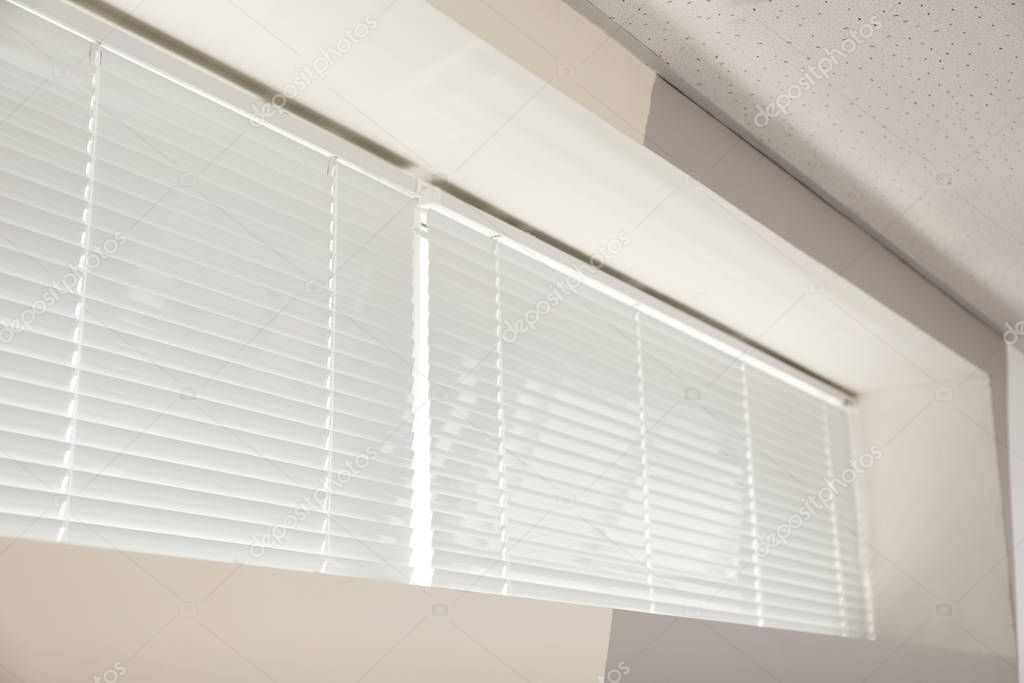 Modern window with closed white blinds indoors