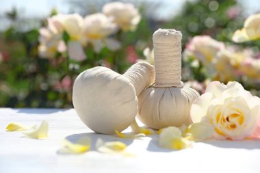 Spa masaj bitkisel çanta, gül ve çiçeklenme bahçede beyaz masada yaprakları. Uyum ve zen