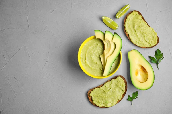 Platte lay samenstelling met Bowl van guacamole gemaakt van rijpe avocado's op grijze tafel. Ruimte voor tekst — Stockfoto