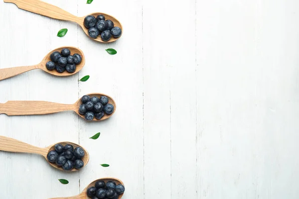 Poser à plat la composition des cuillères avec des bleuets savoureux et des feuilles sur une table en bois blanc, espace pour le texte — Photo