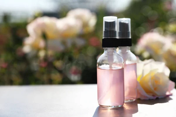 Bottles of facial toner with essential oil and fresh rose on table against blurred background. Space for text — Stock Photo, Image