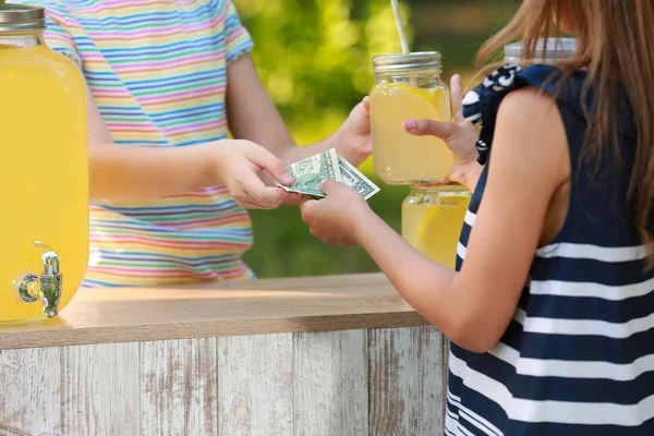 Little girl selling natural lemonade to kid in park, closeup. Summer refreshing drink — Stock Photo, Image