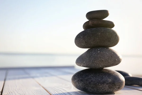 Montón de piedras oscuras en la cubierta de madera cerca del mar. Concepto zen — Foto de Stock