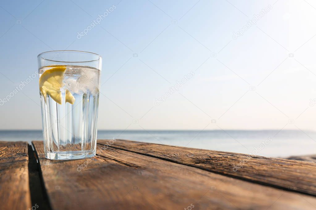 Wooden table with glass of refreshing lemon drink on hot summer day outdoors, space for text