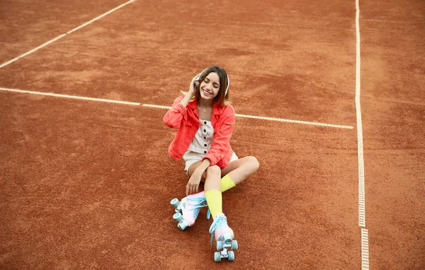 Feliz mujer joven con estilo con patines de ruedas vintage y auriculares sentados en la cancha de tenis —  Fotos de Stock