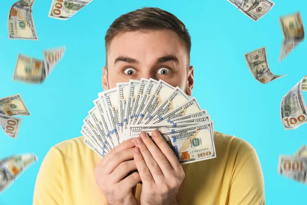 Emotional young man with dollars under money rain on blue background — Stock Photo, Image