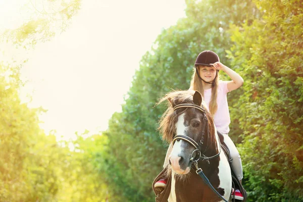 Cute little girl riding pony in park on sunny day — Stock Photo, Image