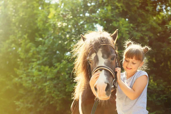 Милая маленькая девочка со своим пони в парке в солнечный день — стоковое фото