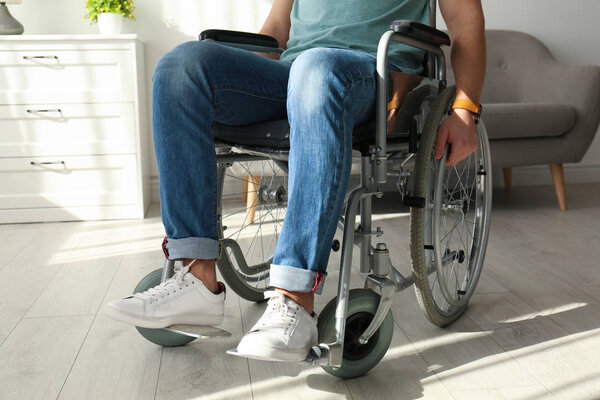 Молодой человек сидит в инвалидной коляске в помещении, крупным планом
