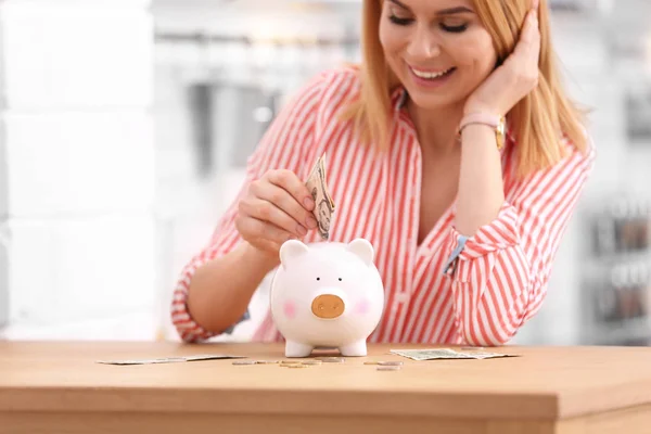 Mulher com banco porquinho e dinheiro em casa — Fotografia de Stock