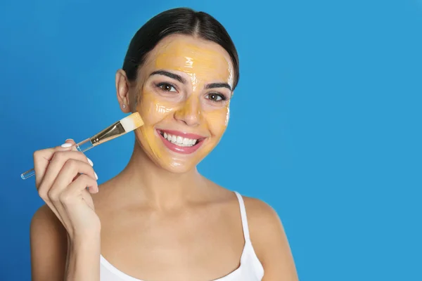 Jonge vrouw die reinigings masker toepast op haar gezicht tegen kleur achtergrond. Ruimte voor tekst — Stockfoto