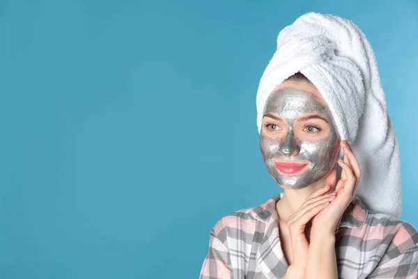 Young woman with cleansing mask on her face against color background, space for text. Skin care