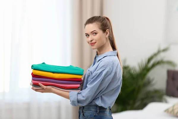Kvinna håller vikta rena kläder i sovrummet. Tvätt dag — Stockfoto