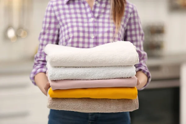 Woman holding stack of colorful towels in kitchen, closeup. Laundry day — Stock Photo, Image