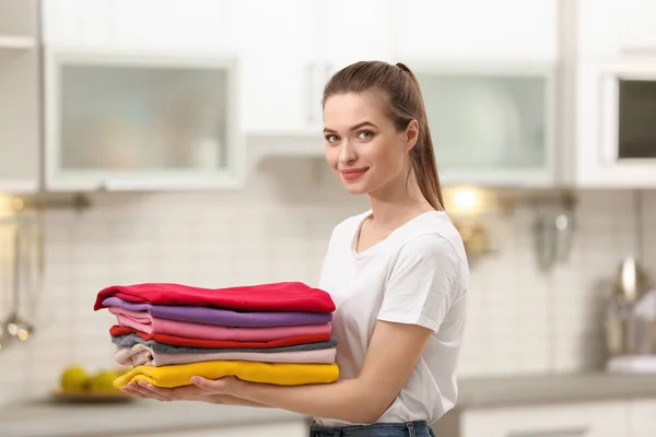 Kobieta trzyma składane czyste ubrania w kuchni. Dzień prania — Zdjęcie stockowe