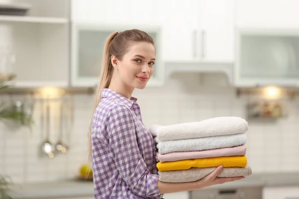 Женщина держит сложенные чистые полотенца на кухне. День прачечной — стоковое фото