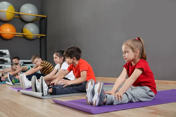 Lindos niños pequeños sentados en el suelo y haciendo ejercicio físico en el gimnasio de la escuela. Estilo de vida saludable —  Fotos de Stock