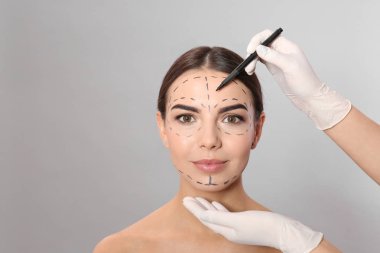 Doktor gri arka plan karşı kozmetik cerrahi operasyon için kadının yüzüne işaretler çizim