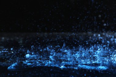 Karanlık arka plana karşı yere düşen ağır yağmur, mavi tonlu