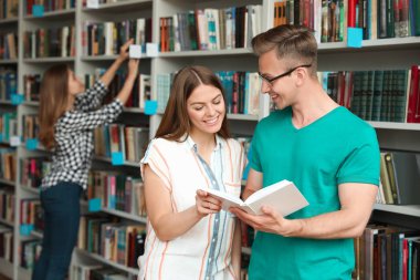 Kütüphanede kitaplıkların yanında duran gençler