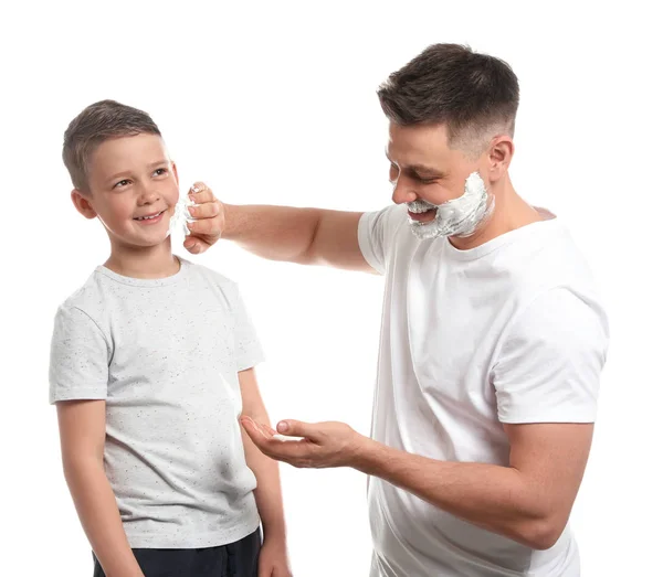 Papa trägt Rasierschaum auf dem Gesicht des Sohnes auf, weißer Hintergrund — Stockfoto