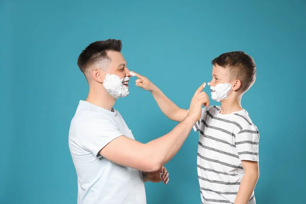 Gelukkige vader en zoon met scheerschuim op gezichten tegen blauwe achtergrond — Stockfoto