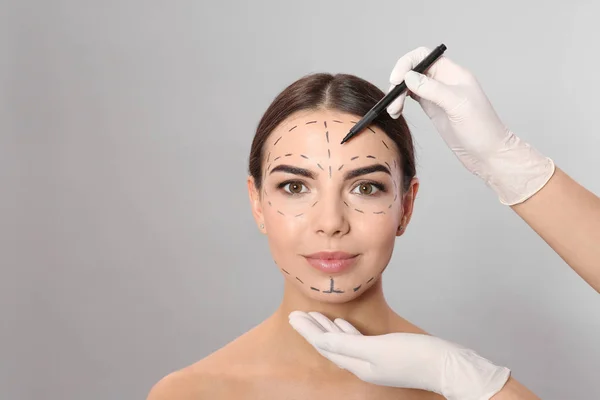 Arts tekenen Marks op gezicht van de vrouw voor cosmetische chirurgie operatie tegen grijze achtergrond — Stockfoto