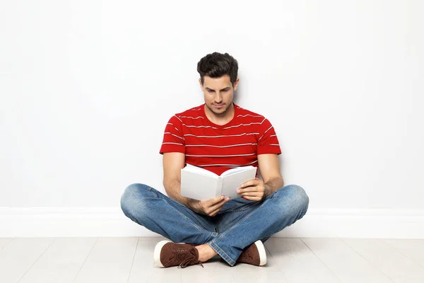 Schöner Mann liest Buch auf dem Fußboden neben weißer Wand — Stockfoto
