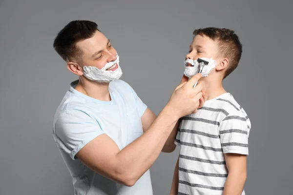 Papá fingiendo afeitar a su hijo con navaja de afeitar sobre fondo gris — Foto de Stock