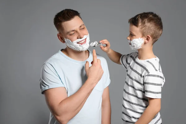 Zoon scheerschuim toepassen op papa's gezicht, grijze achtergrond — Stockfoto