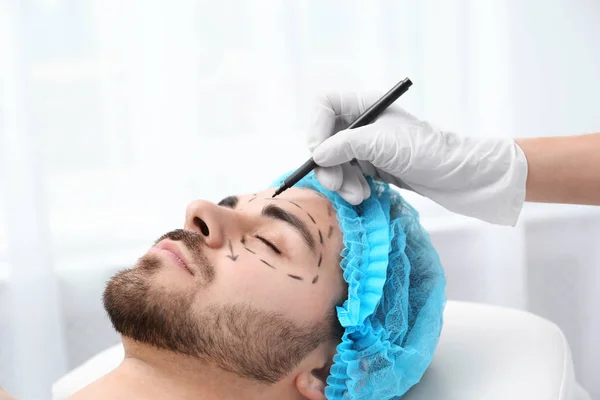 Doctor drawing marks on man's face for cosmetic surgery operation in clinic — Stock Photo, Image