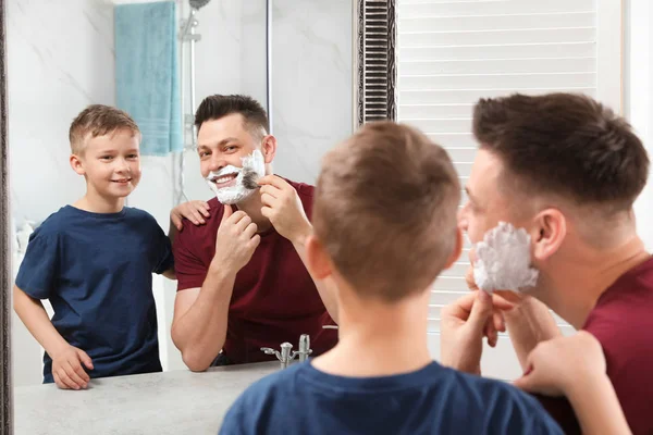 Papa toepassen scheerschuim in de buurt van zoon in spiegel in badkamer — Stockfoto