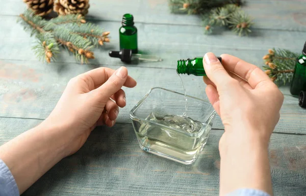 Mujer vertiendo aceite esencial en el tazón de la botella en la mesa, primer plano — Foto de Stock