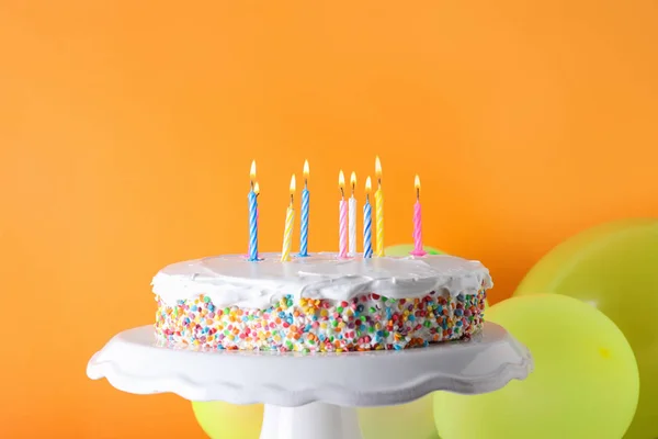 Sabroso pastel de cumpleaños con velas encendidas y globos sobre fondo naranja —  Fotos de Stock