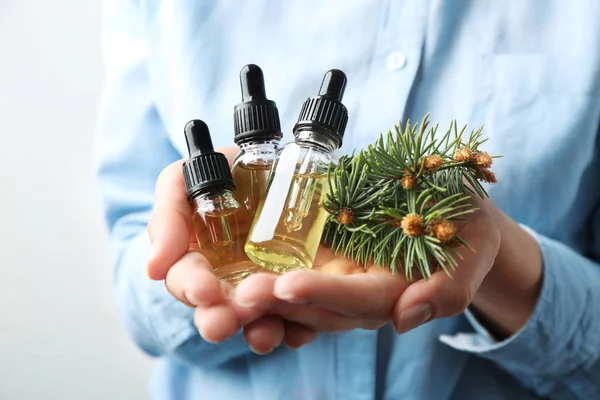 Mujer sosteniendo botellas de aceites esenciales y ramas de abeto sobre fondo blanco, primer plano — Foto de Stock