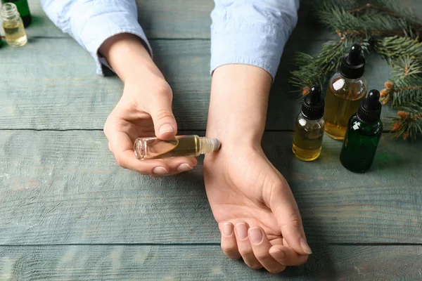 Woman applying essential oil on wrist at wooden table, closeup — Stock Photo, Image