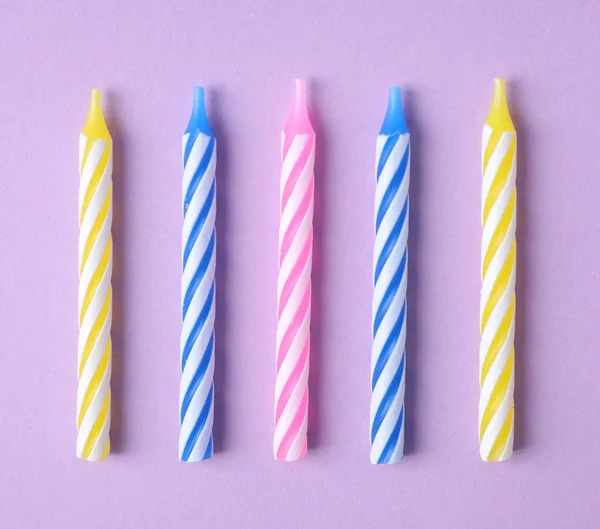 Leylak arka plan üzerinde renkli çizgili doğum günü mumları, düz yatıyordu