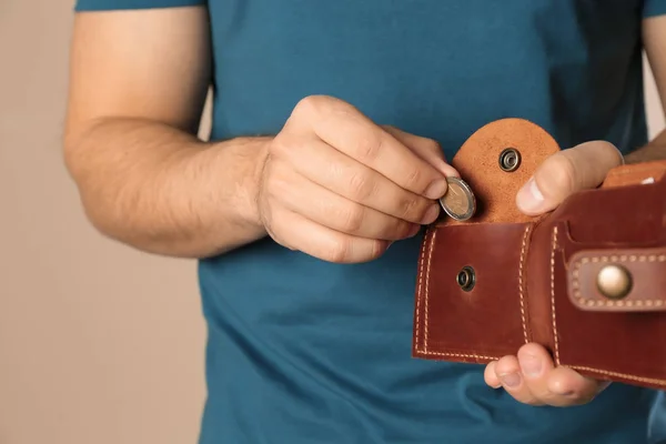 Молодий чоловік кладе монету в гаманець на бежевому тлі, крупним планом. Простір для тексту — стокове фото