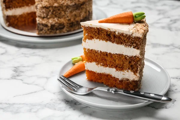 Piece of sweet carrot cake with delicious cream on white marble table