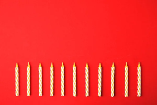 Velas de aniversário listradas amarelas no fundo vermelho, vista superior com espaço para texto — Fotografia de Stock
