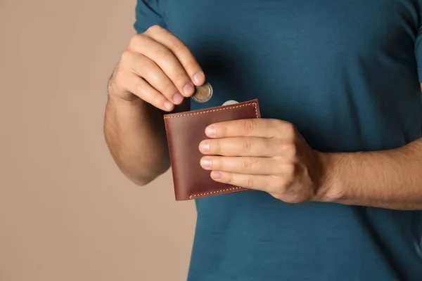 Молодой человек кладет монету в бумажник на бежевом фоне, крупным планом — стоковое фото