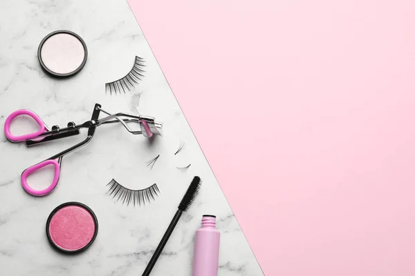 Flat lay composition with false eyelashes and other makeup products on color background, space for text