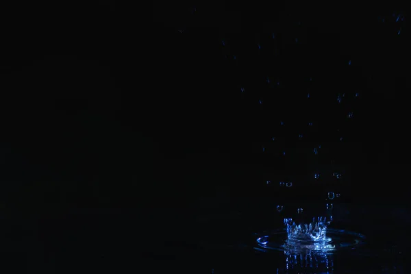 Rain drop falling down into puddle on dark background, space for text