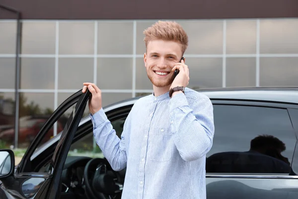 Atraktivní mladík hovořík o telefonu poblíž auta — Stock fotografie