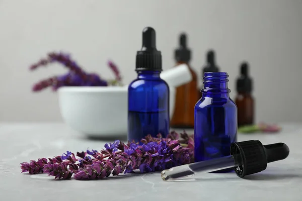 Garrafas de sálvia óleo essencial e flores na mesa cinza — Fotografia de Stock