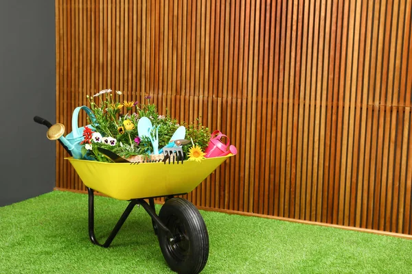 Інвалідний візок з квітами та садовими інструментами біля дерев'яної стіни. Простір для тексту — стокове фото