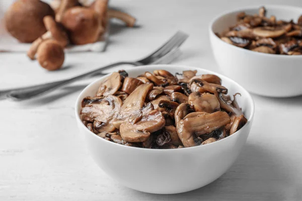 Bowl with delicious cooked mushrooms on white wooden table