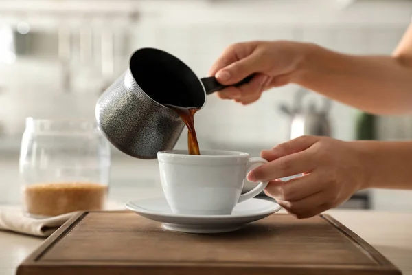 Wanita menuangkan kopi segar ke dalam cangkir di meja dapur, closeup — Stok Foto